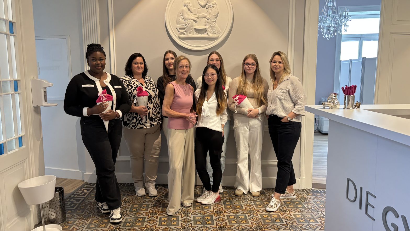 Acht Frauen stehen in einem freundlich eingerichteten Empfangsbereich und lächeln in die Kamera. Einige halten Geschenke in den Händen.